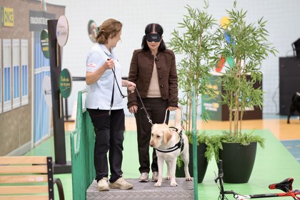 Carolina Darias, con antifaz, guiada por uno de los perros de la exhibición y una instrutora de la FOPG