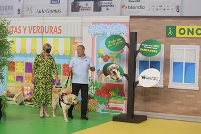 La presidenta del Parlamento de Cantabria, María José González, con antifaz, se deja guiar por uno de los perros y su instructo