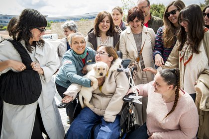 Imagen de noticia: Personal de las direcciones generales de Derechos de las Personas con Discapacidad y de los Animales, visitan la Fundación ONCE del Perro Guía Grupo de visitantes junto a un cachorro que es cogido por una de las trabajadoras
