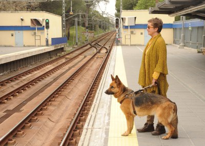 Una usuaria con su perro guía esperando el metro en el andén